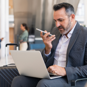 A professional businessman at an airport using a smartphone and laptop, showcasing the convenience of virtual mailbox services for travelers.